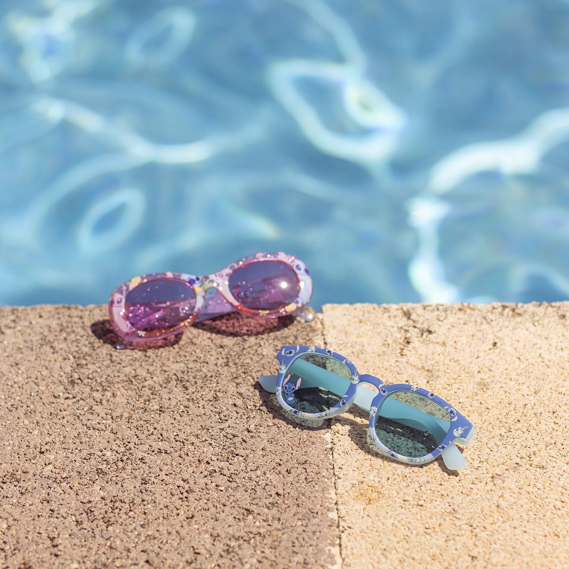 Óculos de sol infantis rosa e azul com detalhes divertidos ao lado de uma piscina